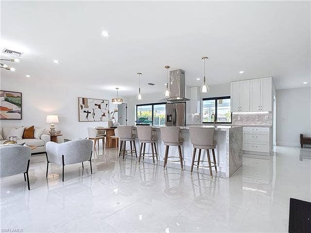 125 41st Ter, Cape Coral, FL 33904 Kitchen with stainless steel fridge, a breakfast bar area, white cabinets, decorative backsplash, and hanging light fixtures