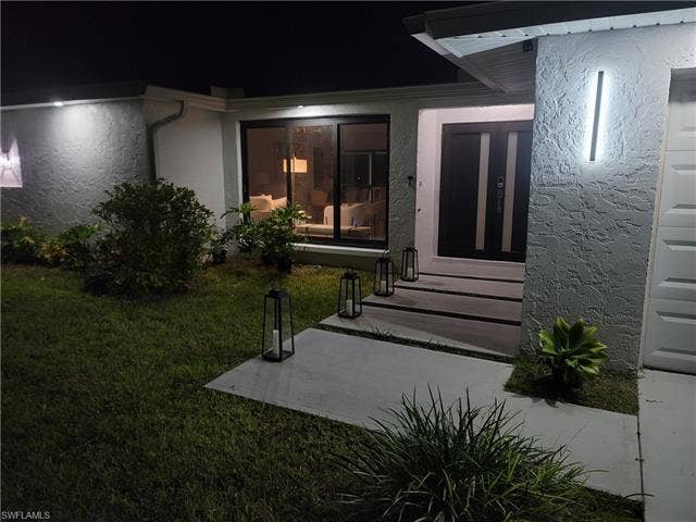 125 41st Ter, Cape Coral, FL 33904 Exterior entry at twilight with a yard and stucco siding
