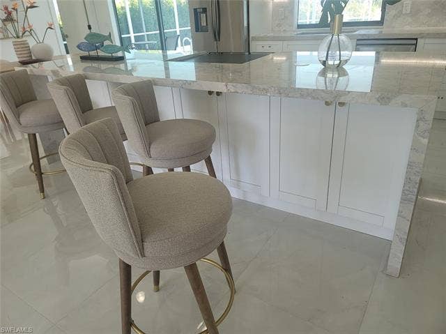 125 41st Ter, Cape Coral, FL 33904 Kitchen featuring white cabinetry, light stone counters, stainless steel fridge with ice dispenser, and a kitchen bar