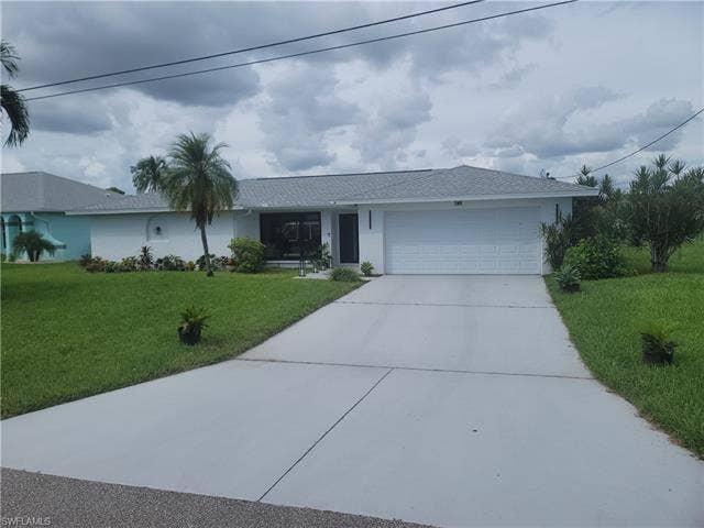 125 41st Ter, Cape Coral, FL 33904 Single story home with driveway, a front yard, stucco siding, an attached garage, and a shingled roof