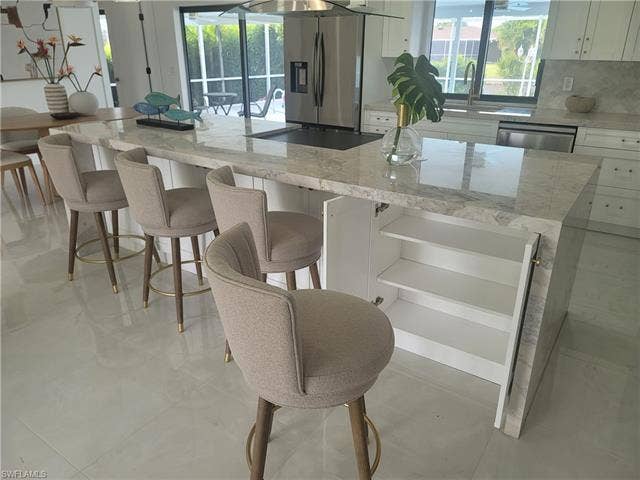 125 41st Ter, Cape Coral, FL 33904 Kitchen with light stone countertops, white cabinetry, a kitchen island, and a kitchen bar