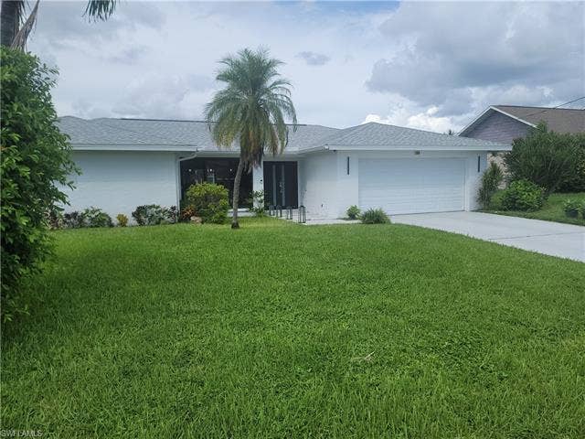 125 41st Ter, Cape Coral, FL 33904 Ranch-style house featuring stucco siding, concrete driveway, a front lawn, and an attached garage