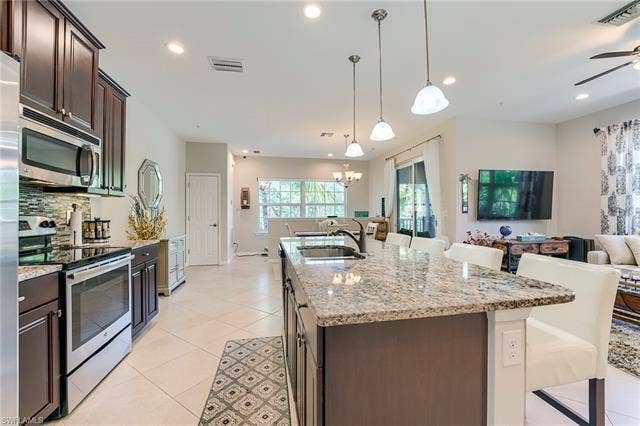 8510 Violeta St, #203, Estero, FL 34135 Kitchen featuring appliances with stainless steel finishes, dark brown cabinetry, light stone counters, a kitchen breakfast bar, and light tile patterned flooring