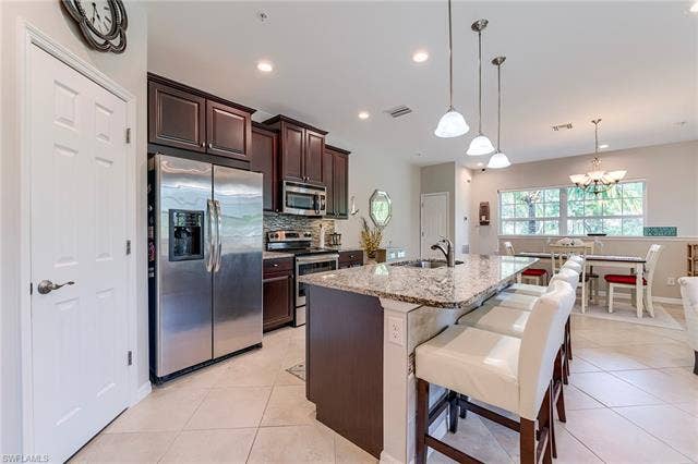 8510 Violeta St, #203, Estero, FL 34135 Kitchen with dark brown cabinets, appliances with stainless steel finishes, light stone counters, pendant lighting, and an island with sink