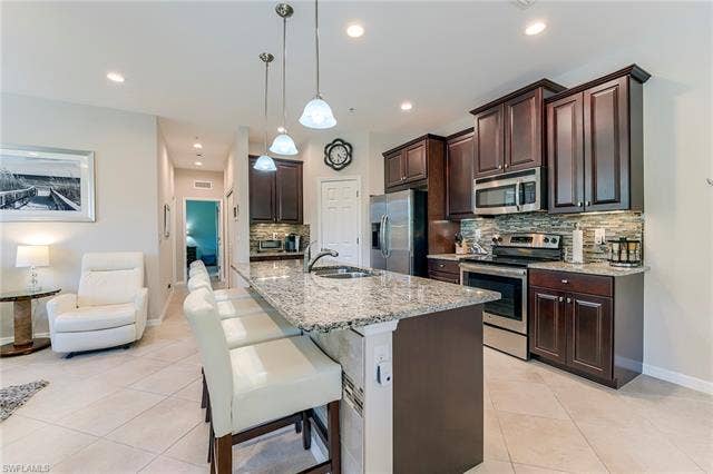 8510 Violeta St, #203, Estero, FL 34135 Kitchen featuring dark brown cabinetry, tasteful backsplash, appliances with stainless steel finishes, light stone countertops, and a kitchen breakfast bar