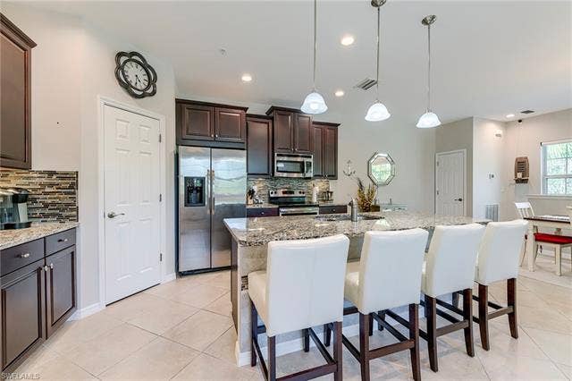 8510 Violeta St, #203, Estero, FL 34135 Kitchen featuring stainless steel appliances, dark brown cabinetry, light stone countertops, hanging light fixtures, and a breakfast bar area