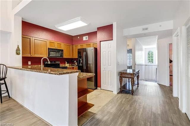10127 Villagio Palms Way, #203, Estero, FL 33928 Kitchen with black appliances, dark stone countertops, light wood finished floors, a peninsula, and open shelves