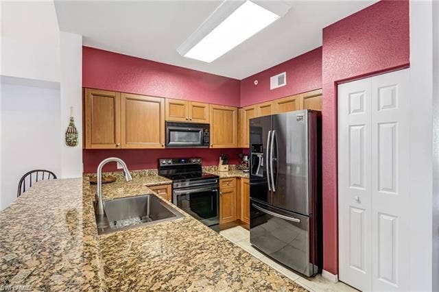 10127 Villagio Palms Way, #203, Estero, FL 33928 Kitchen featuring a peninsula, stainless steel appliances, a textured wall, light stone counters, and light tile patterned floors