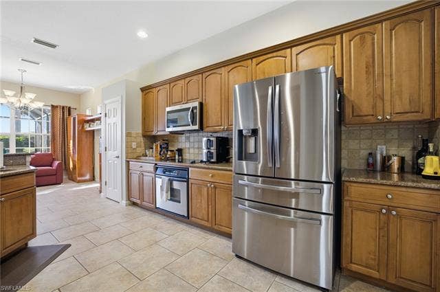 22140 Long Leaf Trail Dr, Estero, FL 34135 Kitchen featuring appliances with stainless steel finishes, brown cabinets, dark stone countertops, a chandelier, and hanging light fixtures