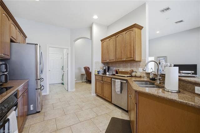 22140 Long Leaf Trail Dr, Estero, FL 34135 Kitchen with stainless steel appliances, dark stone countertops, arched walkways, backsplash, and light tile patterned floors