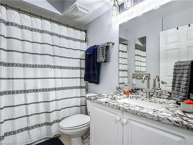 25735 Lake Amelia Way, #103, Bonita Springs, FL 34135 Bathroom featuring vanity, curtained shower, and a textured ceiling