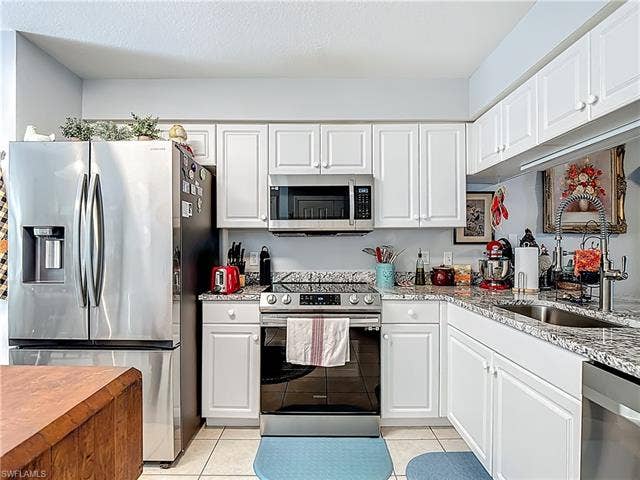 25735 Lake Amelia Way, #103, Bonita Springs, FL 34135 Kitchen featuring stainless steel appliances, light stone counters, white cabinetry, and light tile patterned floors