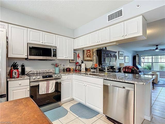 25735 Lake Amelia Way, #103, Bonita Springs, FL 34135 Kitchen with white cabinets, appliances with stainless steel finishes, light stone counters, ceiling fan, and light tile patterned floors