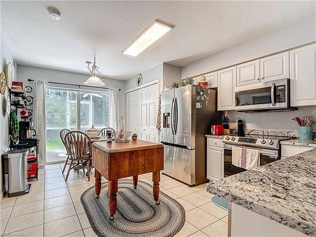 25735 Lake Amelia Way, #103, Bonita Springs, FL 34135 Kitchen featuring stainless steel appliances, light stone countertops, light tile patterned flooring, white cabinets, and a textured ceiling