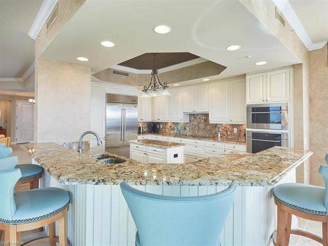 23750 Via Trevi Way, #2001, Estero, FL 34134 Kitchen featuring ornamental molding, a breakfast bar, a raised ceiling, light stone countertops, and stainless steel appliances