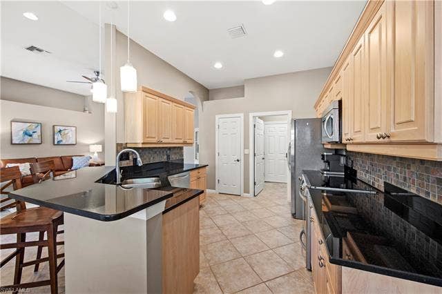 14546 Speranza Way, Bonita Springs, FL 34135 Kitchen featuring light brown cabinets, appliances with stainless steel finishes, backsplash, a breakfast bar, and light tile patterned floors