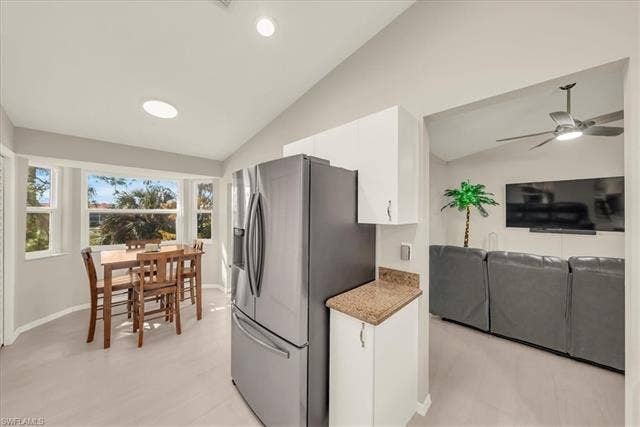 7320 Glenmoor Ln, #2304, Naples, FL 34104 Kitchen with vaulted ceiling, stainless steel fridge with ice dispenser, white cabinetry, open floor plan, and light stone counters