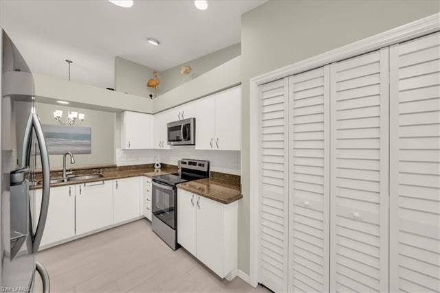7320 Glenmoor Ln, #2304, Naples, FL 34104 Kitchen featuring appliances with stainless steel finishes, white cabinets, dark stone counters, and a chandelier