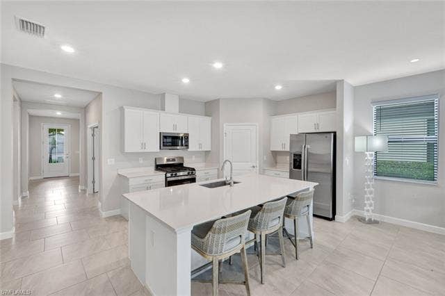 18298 Ridgeline Dr, Estero, FL 33928 Kitchen with white cabinets, stainless steel appliances, a breakfast bar area, a kitchen island with sink, and recessed lighting