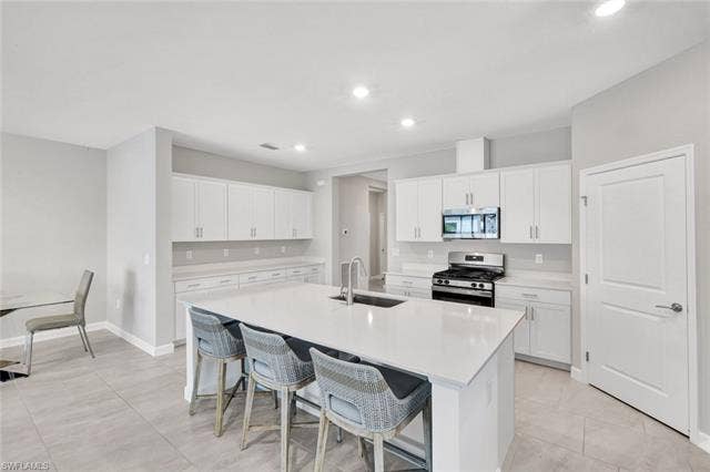 18298 Ridgeline Dr, Estero, FL 33928 Kitchen featuring stainless steel appliances, a kitchen breakfast bar, white cabinetry, an island with sink, and light stone countertops