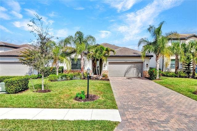 18298 Ridgeline Dr, Estero, FL 33928 Ranch-style home featuring decorative driveway, a garage, a front lawn, a tile roof, and stucco siding