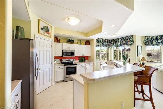 20667 Wildcat Run Dr, #101, Estero, FL 33928 Kitchen featuring stainless steel appliances, a kitchen island with sink, light countertops, a breakfast bar, and white cabinets