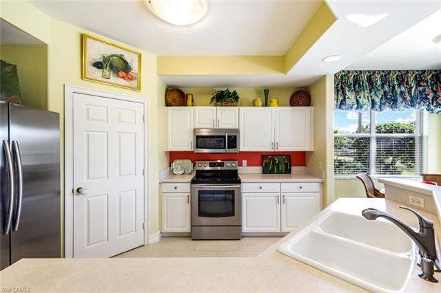 20667 Wildcat Run Dr, #101, Estero, FL 33928 Kitchen with stainless steel appliances, white cabinetry, light countertops, and light tile patterned floors
