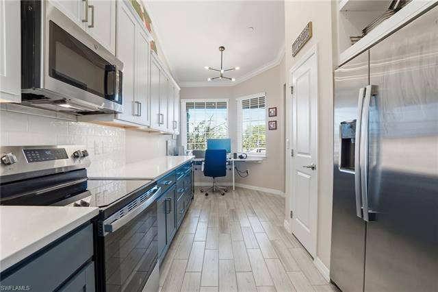 11861 Venetian Lagoon Dr, #203, Fort Myers, FL 33913 Dual tone kitchen with stainless steel appliances, ornamental molding, wood finish floors, tasteful backsplash, and hanging lights