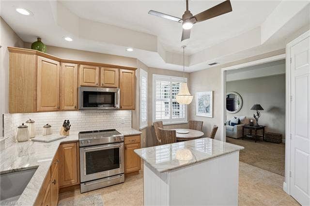 19620 Marino Lake Cir, #2802, Miromar Lakes, FL 33913 Kitchen featuring a tray ceiling, stainless steel appliances, light stone countertops, a ceiling fan, and decorative light fixtures