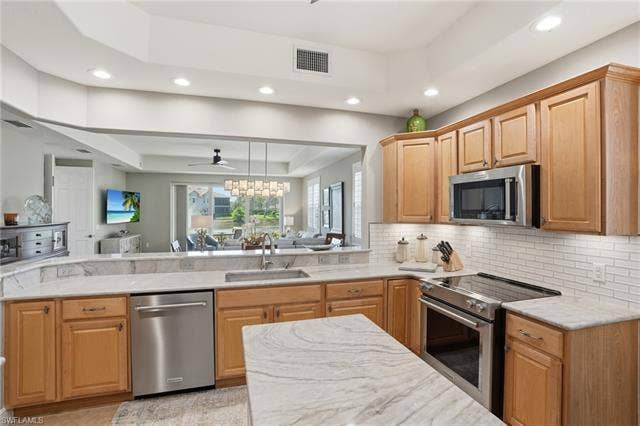 19620 Marino Lake Cir, #2802, Miromar Lakes, FL 33913 Kitchen featuring a tray ceiling, stainless steel appliances, light stone counters, a ceiling fan, and open floor plan