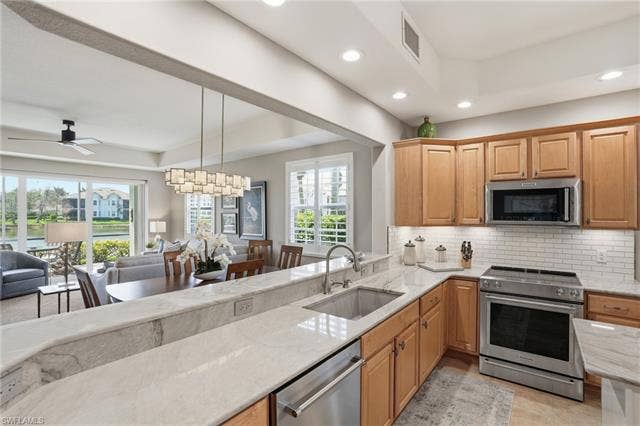 19620 Marino Lake Cir, #2802, Miromar Lakes, FL 33913 Kitchen featuring stainless steel appliances, open floor plan, light stone counters, a ceiling fan, and a raised ceiling