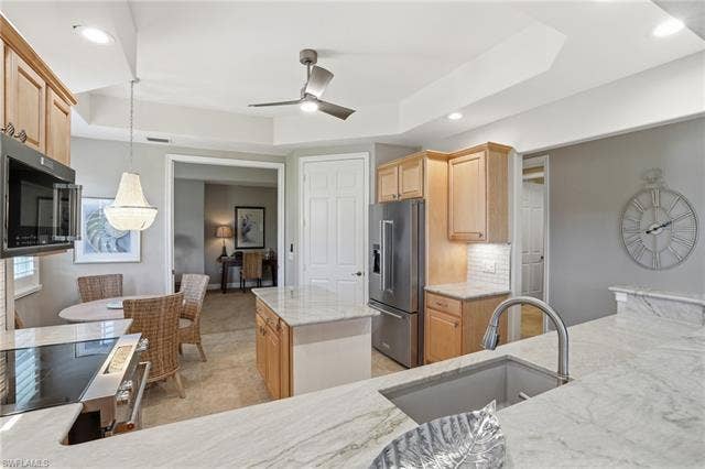 19620 Marino Lake Cir, #2802, Miromar Lakes, FL 33913 Kitchen featuring a raised ceiling, stainless steel appliances, light wood finish cabinets, tasteful backsplash, and light stone countertops
