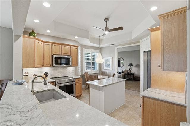 19620 Marino Lake Cir, #2802, Miromar Lakes, FL 33913 Kitchen with a raised ceiling, stainless steel appliances, light wood finish cabinetry, a center island, and a ceiling fan