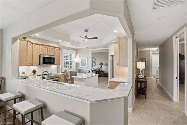 19620 Marino Lake Cir, #2802, Miromar Lakes, FL 33913 Kitchen with a kitchen island, light wood finish cabinetry, backsplash, a ceiling fan, and light stone counters