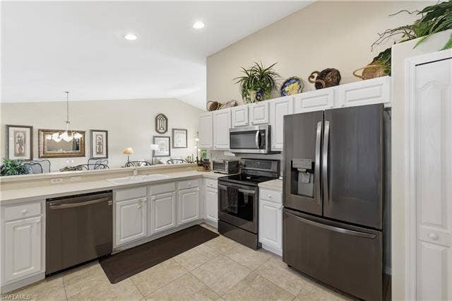 23541 Sandycreek Ter, #806, Estero, FL 34135 Kitchen with stainless steel appliances, light countertops, white cabinetry, lofted ceiling, and light tile patterned floors