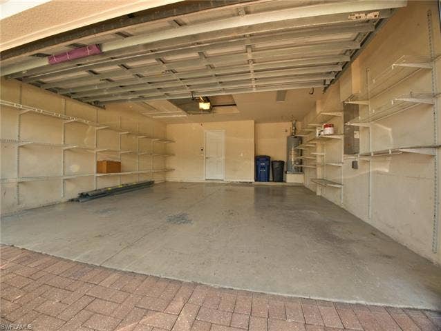 9071 Astonia Way, Estero, FL 33967 Spacious garage featuring extensive built-in shelving, a smooth concrete floor, and brick paver driveway entry