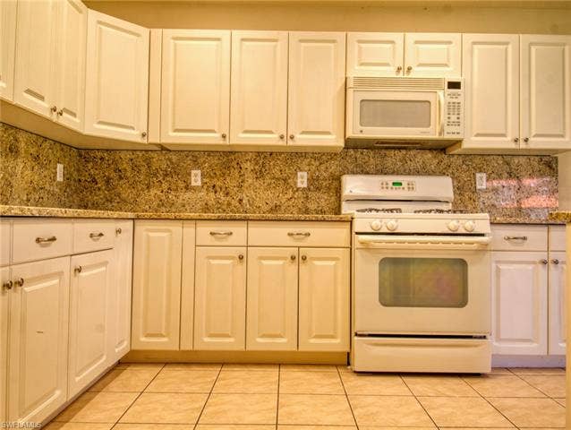 9071 Astonia Way, Estero, FL 33967 Kitchen featuring white cabinetry, stone countertops, integrated microwave, and a white oven/range