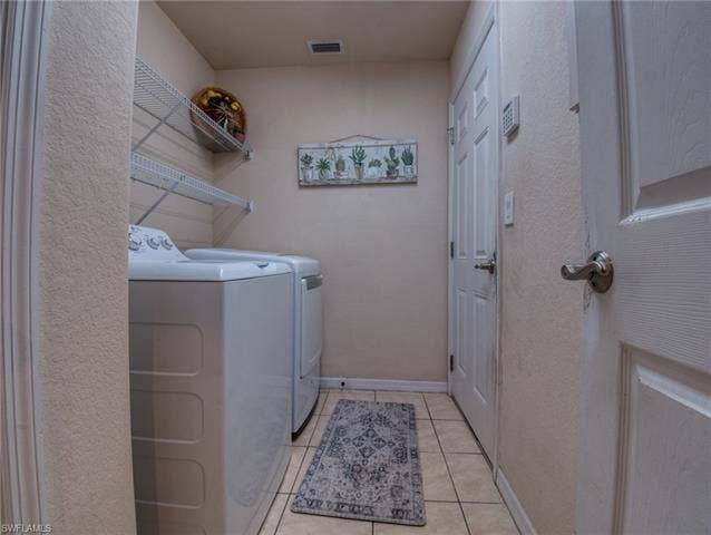 9071 Astonia Way, Estero, FL 33967 Laundry room featuring washer and clothes dryer, light tile patterned floors, and a textured wall