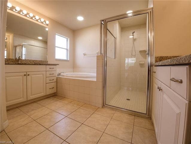 9071 Astonia Way, Estero, FL 33967 Bathroom featuring a tiled floor, dual vanities with granite countertops, a built-in soaking tub, and a separate glass-enclosed shower