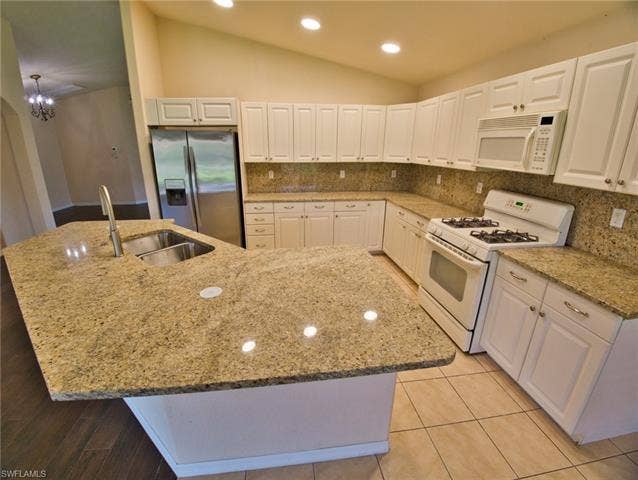 9071 Astonia Way, Estero, FL 33967 Kitchen featuring a large central island with a double basin sink and a high-arc faucet, granite countertops, white cabinetry with silver hardware, a gas range, and tile flooring