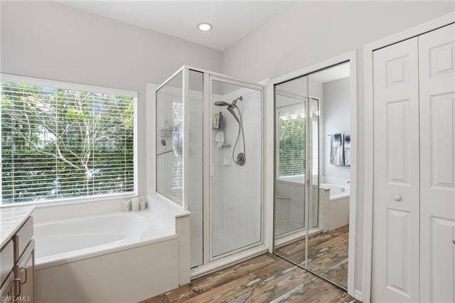 17801 Modena Rd, Miromar Lakes, FL 33913 Bathroom with a garden tub, a stall shower, vanity, a closet, and light wood-type flooring