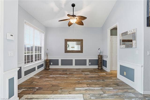17801 Modena Rd, Miromar Lakes, FL 33913 Unfurnished living room with ceiling fan, wood finished floors, a decorative wall, and wainscoting