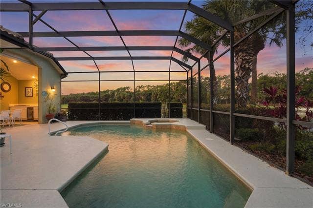 17801 Modena Rd, Miromar Lakes, FL 33913 Pool at dusk featuring a pool with connected hot tub, a lanai, a sunroom, and a patio area
