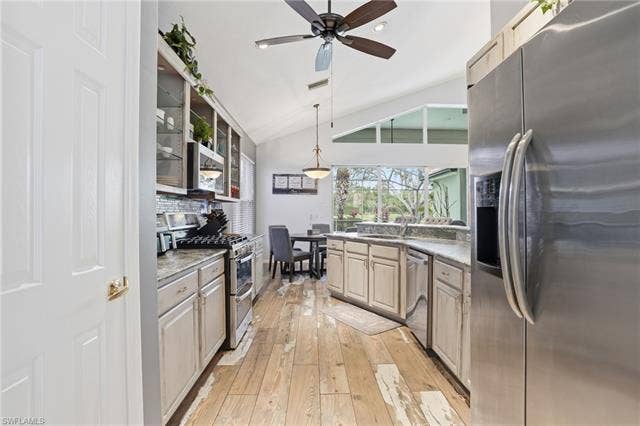 17801 Modena Rd, Miromar Lakes, FL 33913 Kitchen with stainless steel appliances, vaulted ceiling, pendant lighting, light wood finished floors, and glass fronted cabinets