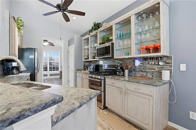17801 Modena Rd, Miromar Lakes, FL 33913 Kitchen featuring stainless steel appliances, light stone counters, vaulted ceiling, light wood finished floors, and decorative backsplash
