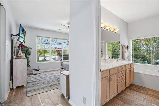 17801 Modena Rd, Miromar Lakes, FL 33913 Ensuite bathroom featuring light wood-style flooring, double vanity, ceiling fan, and plenty of natural light