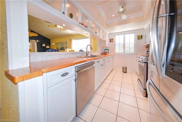 22161 Tallwood Ct, #706, Estero, FL 33928 Galley kitchen featuring white cabinetry with brushed nickel hardware, wood-finish countertops, stainless steel appliances, and a pass-through window