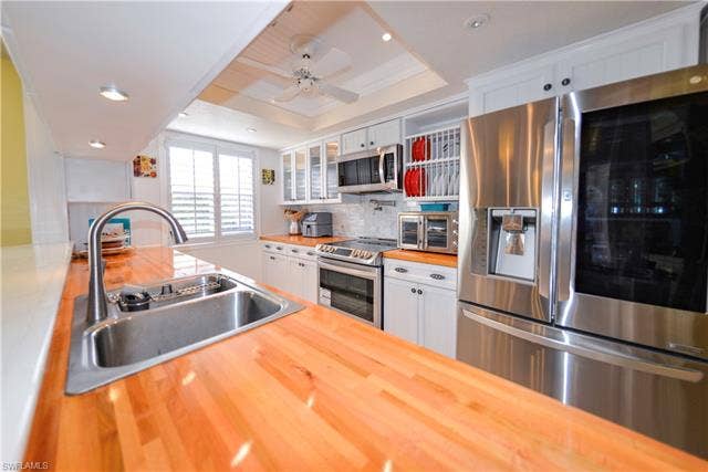 22161 Tallwood Ct, #706, Estero, FL 33928 Kitchen featuring wood-finish countertops, stainless steel appliances, white cabinetry, a dual-basin sink with a gooseneck faucet, and shuttered window coverings