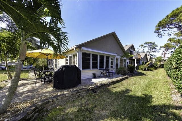 22161 Tallwood Ct, #706, Estero, FL 33928 Exterior featuring a paver patio, mature palm trees, a spacious lawn, and a low stone retaining wall