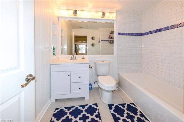 22161 Tallwood Ct, #706, Estero, FL 33928 Bathroom featuring a white vanity with integrated sink, a rectangular mirror, a light fixture with four bulbs, white subway tile walls with a blue accent band, and a white bathtub
